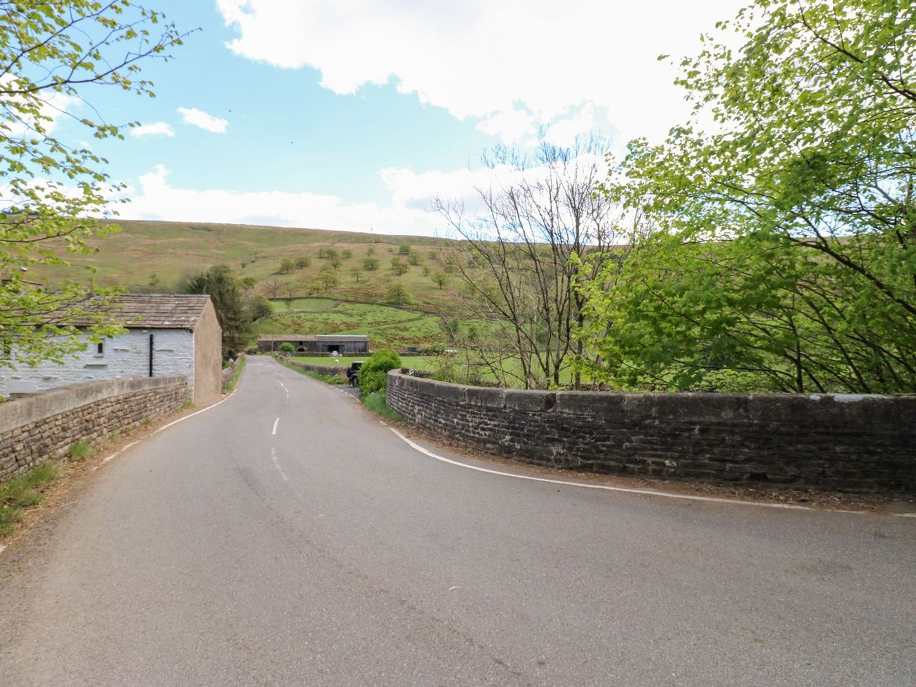 The lane through Garsdale crossing a stone bridge, with field barns and the fellside beyond