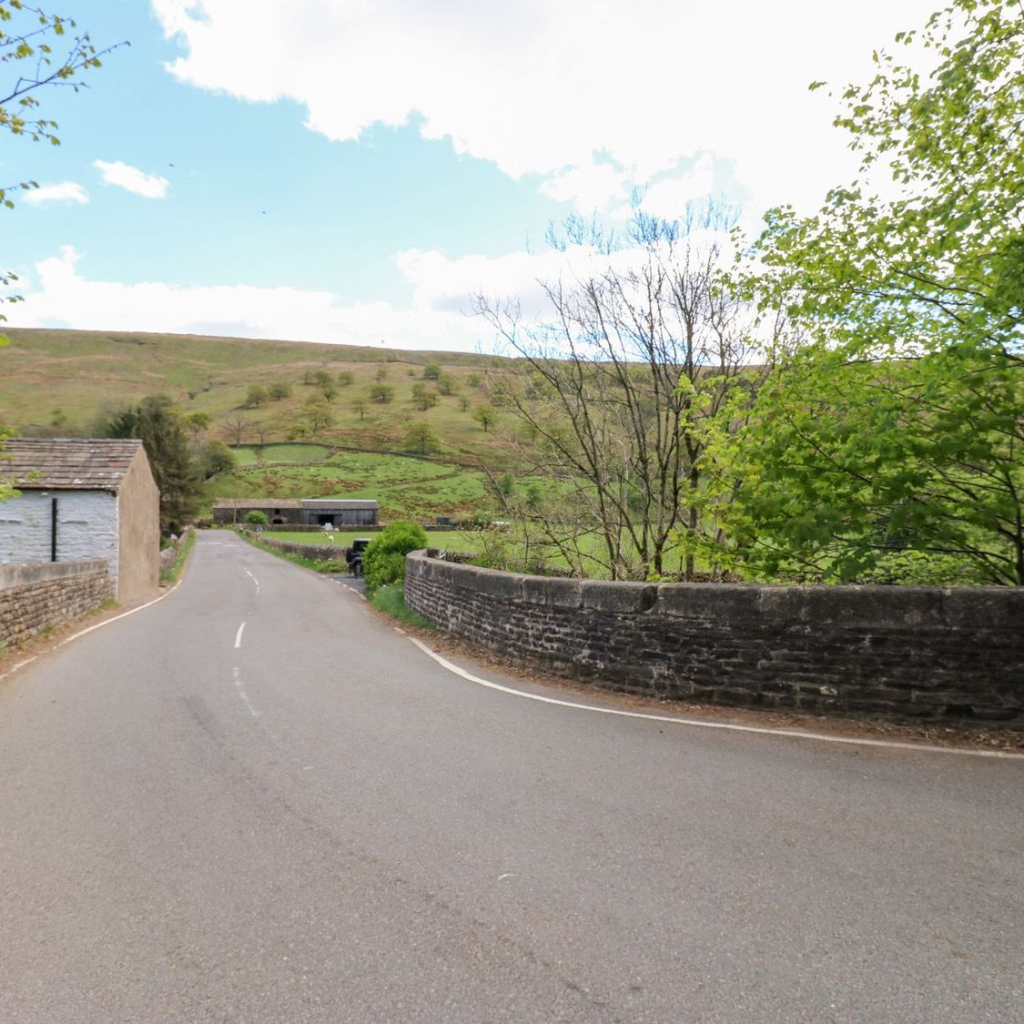 The lane through Garsdale crossing a stone bridge, with field barns and the fellside beyond
