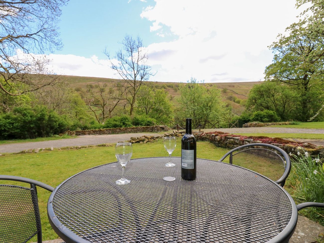A garden table set with a bottle and two glasses at Farrier's Cottage, looking across the valley to the fell