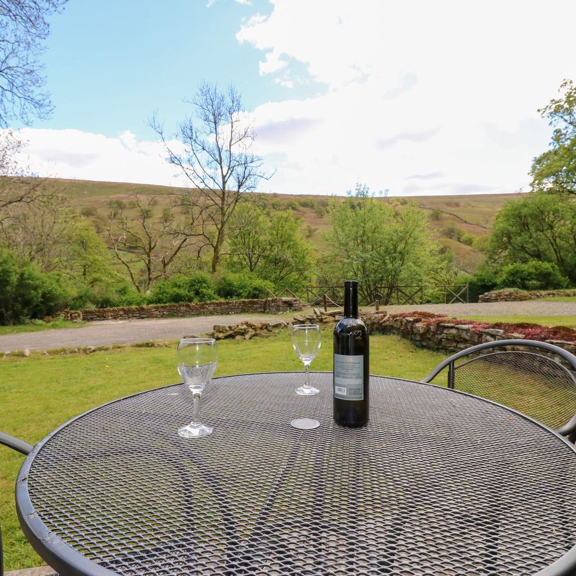 A garden table set with a bottle and two glasses at Farrier's Cottage, looking across the valley to the fell