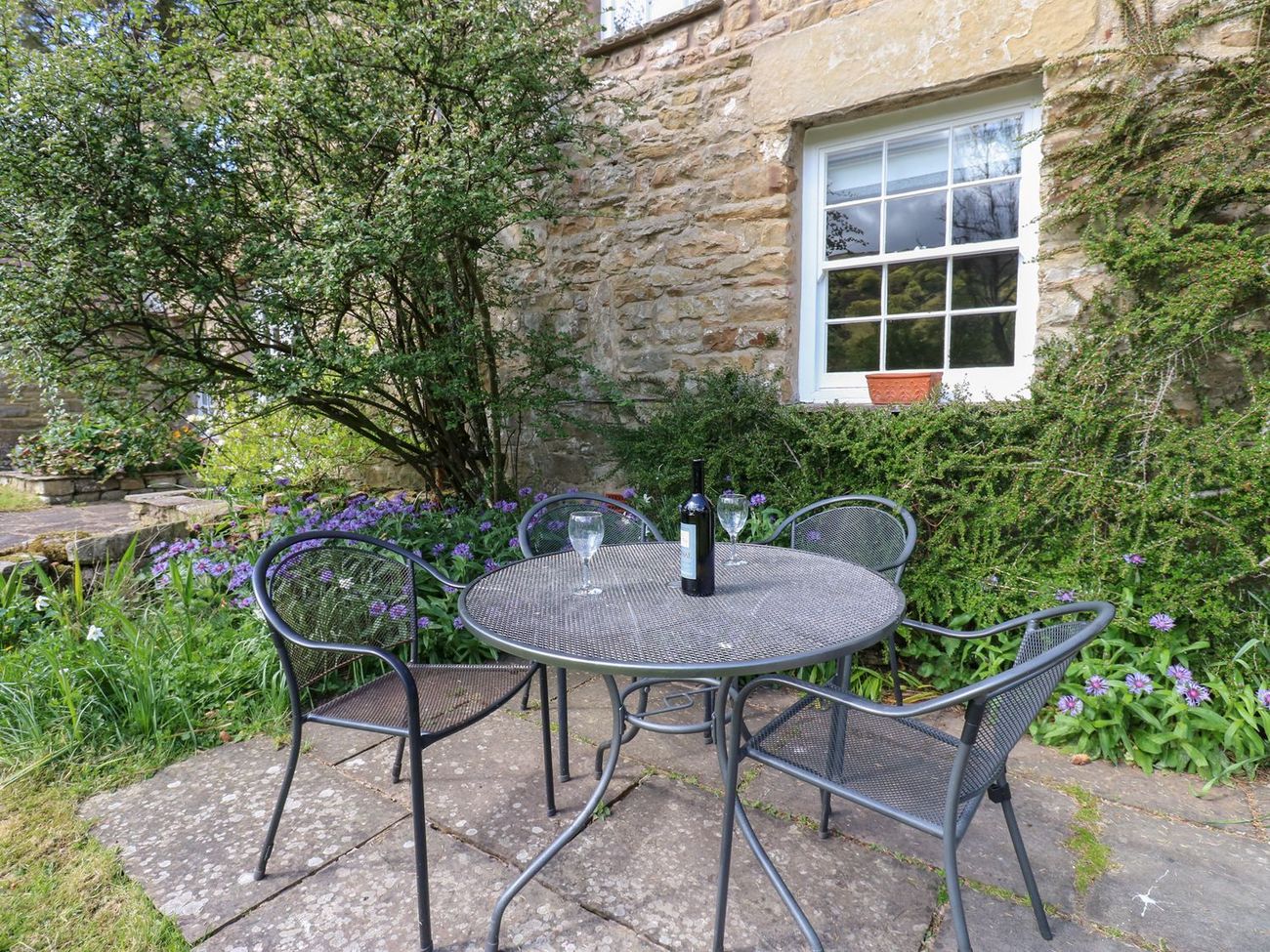 A table and four chairs on the patio at Farrier's Cottage, sheltered by the cottage wall with flowers in the border