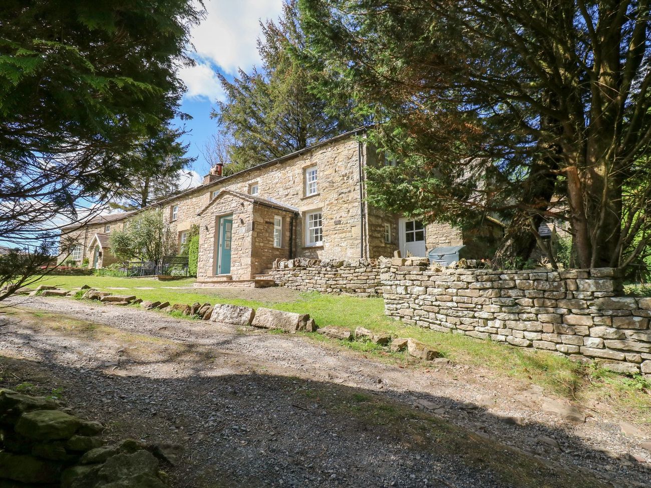 Farrier's Cottage from the track, framed by trees, with dry-stone walls and the lawned garden in front