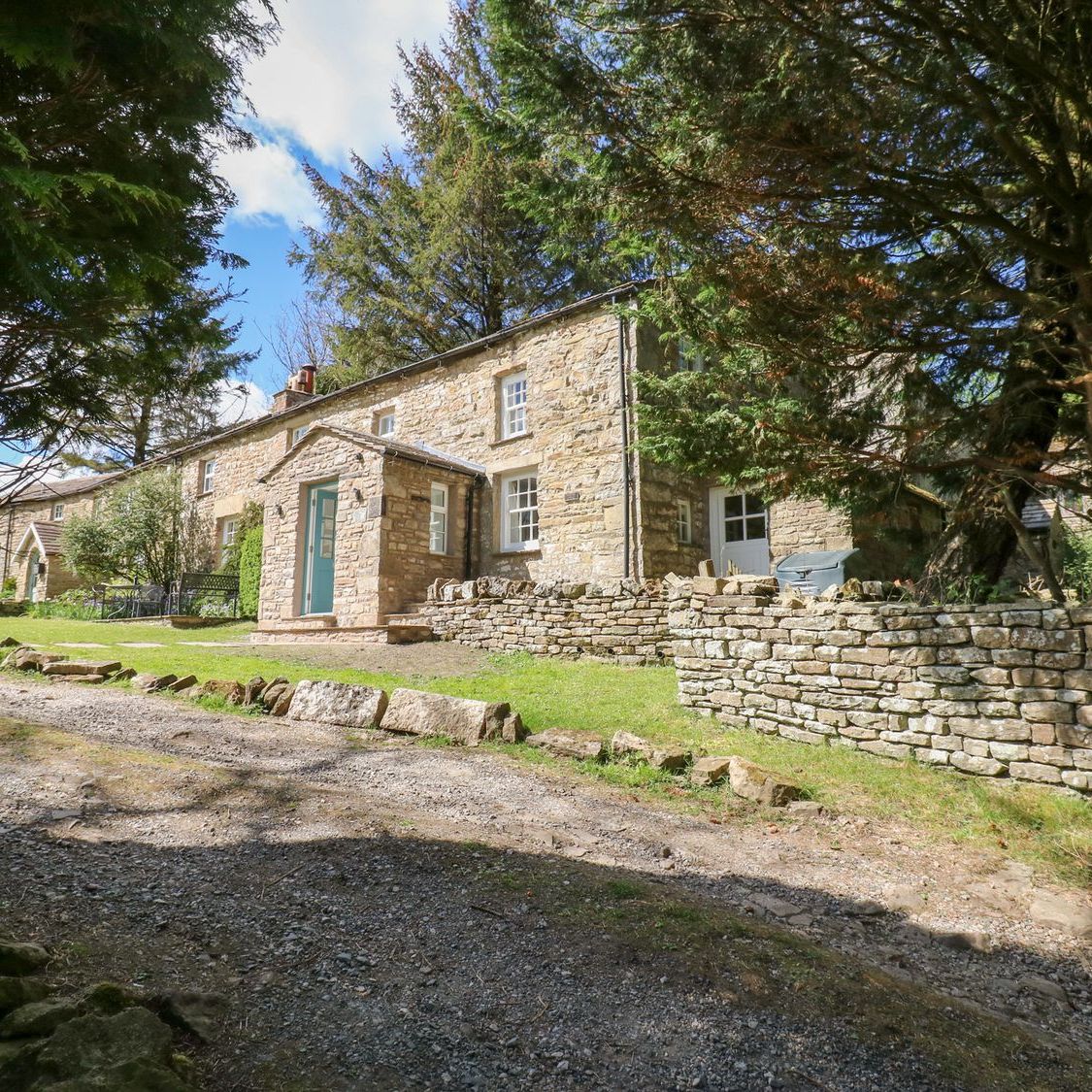 Farrier's Cottage from the track, framed by trees, with dry-stone walls and the lawned garden in front