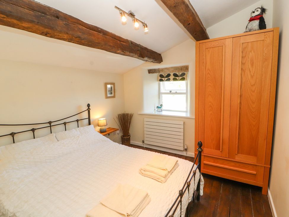 A bedroom with a bed a wooden wardrobe a window and exposed wooden beams at Roger Pot in Garsdale near Sedbergh