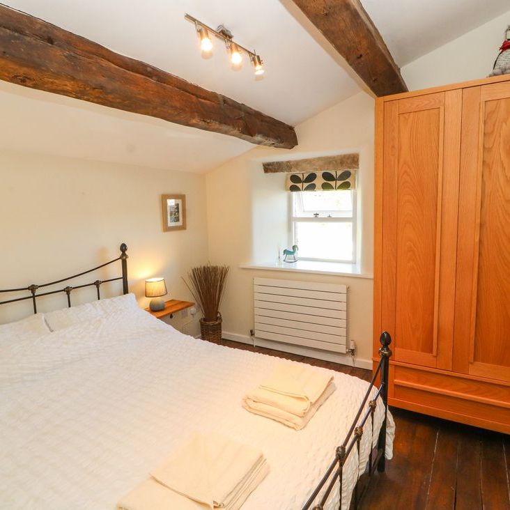 A double bedroom at Roger Pot with a black iron bed, oak wardrobe and exposed ceiling beams