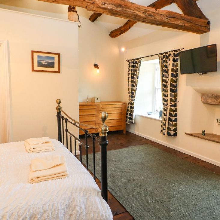 A cottage bedroom at Roger Pot with a black metal bed, wooden dresser, wall-mounted TV and green rug
