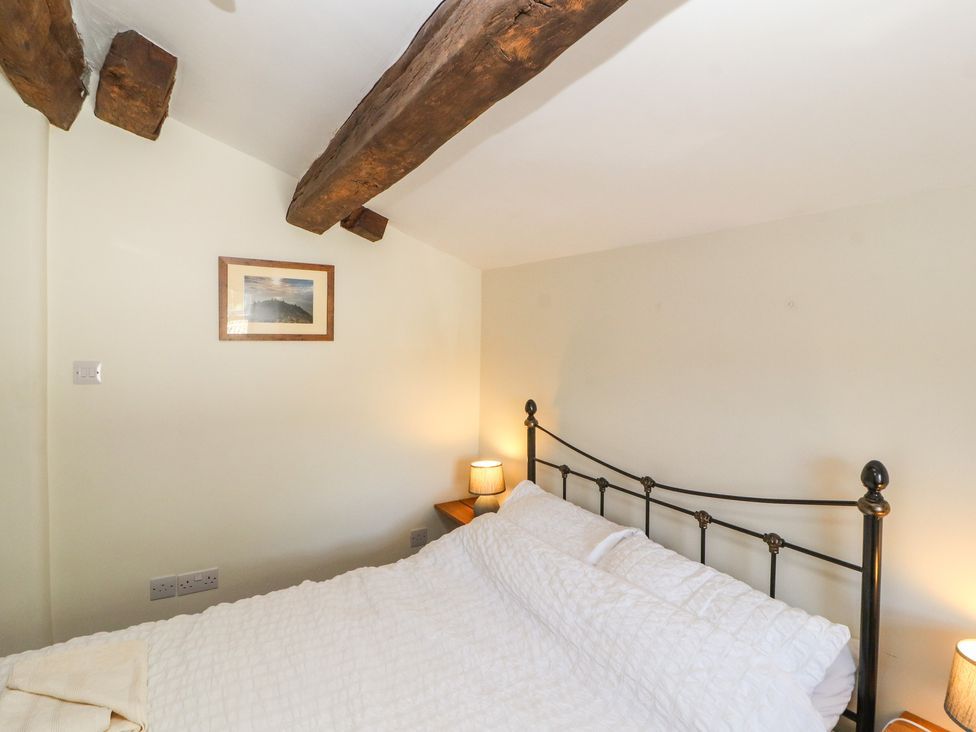 A bedroom with a metal bed frame white bedding wooden ceiling beams and a small bedside lamp at Roger Pot in Garsdale near Sedbergh