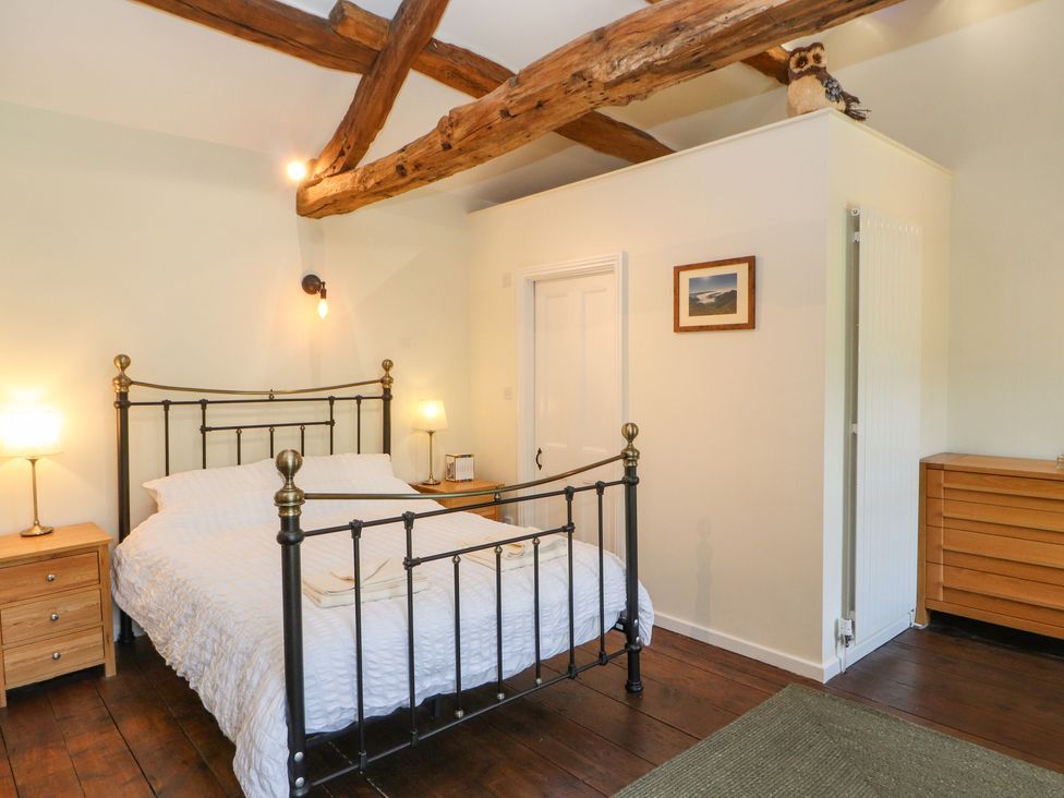 A bedroom with a metal bed frame wooden bedside tables lamps and exposed wooden ceiling beams at Roger Pot in Garsdale near Sedbergh