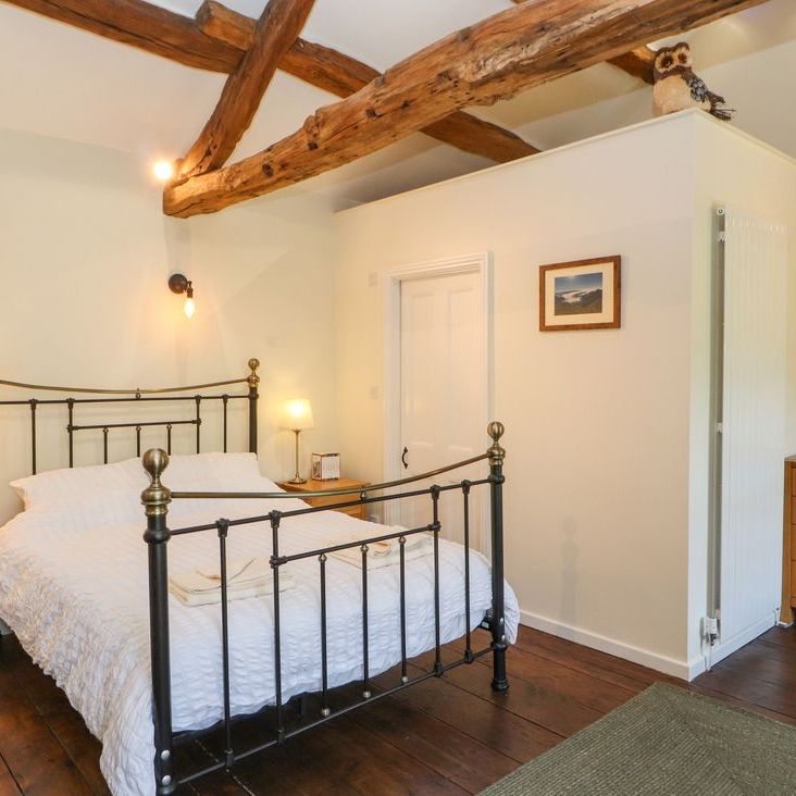 A double bedroom at Roger Pot with a black metal bed, oak bedside tables, lamps and an owl ornament on the wall