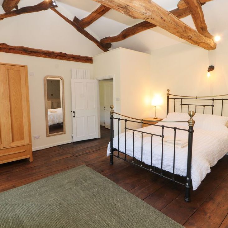 A spacious beamed bedroom at Roger Pot with a black metal double bed, oak wardrobe and full-length mirror