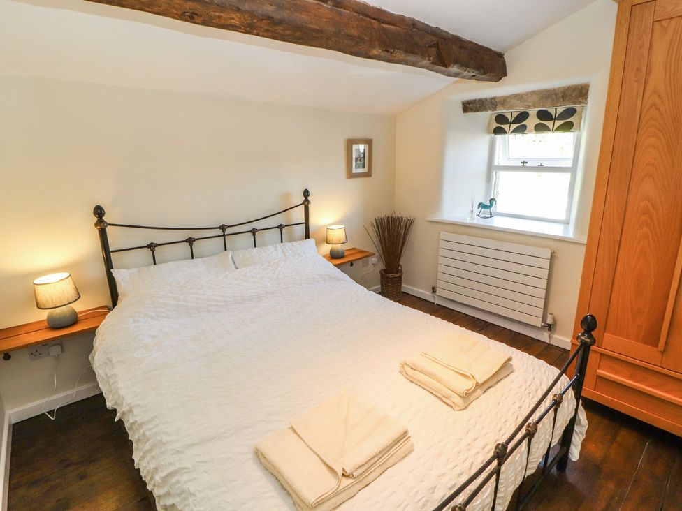 A bedroom with a white bedspread two bedside lamps wooden wardrobe and a window at Roger Pot in Garsdale near Sedbergh