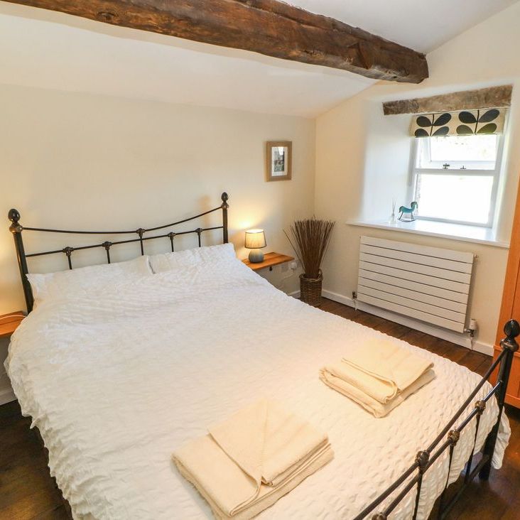 A double bedroom at Roger Pot with a black metal bed, bedside lamps, window seat and oak wardrobe