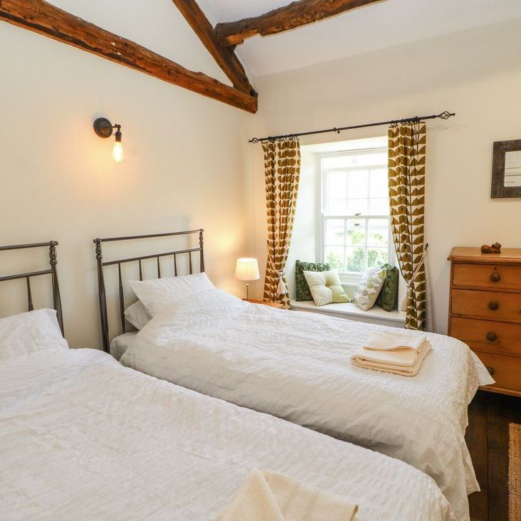 A twin bedroom at Roger Pot with two metal-framed single beds, a cushioned window seat and wooden chest of drawers