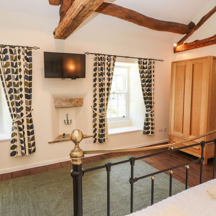 A bright beamed bedroom at Roger Pot with a metal-framed bed, two windows, wall-mounted TV and oak wardrobe