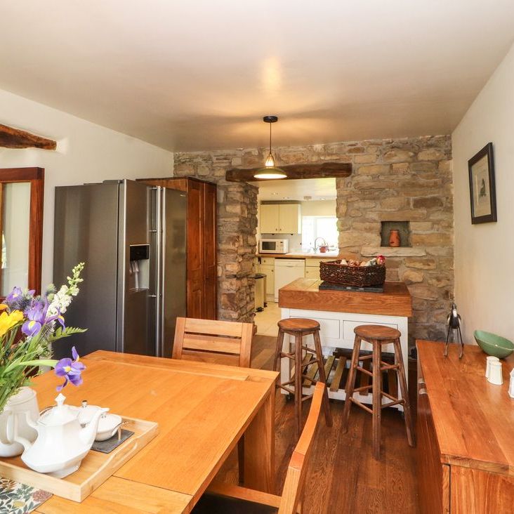 The open-plan dining and kitchen area at Roger Pot with an oak table, stone wall, breakfast bar and fresh flowers