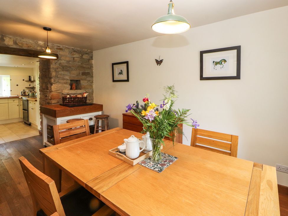 A dining room with wooden table and chairs a vase with flowers and a tray with teapot next to a stone wall opening to a kitchen at Roger Pot in Garsdale near Sedbergh