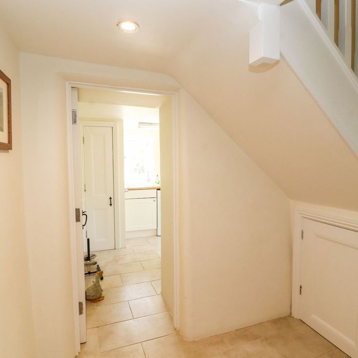 A tiled hallway at Roger Pot with a white staircase, under-stair cupboard and an open doorway to the kitchen