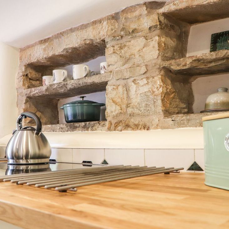 A close-up of the Roger Pot kitchen worktop with stainless-steel kettles on the hob and a rustic stone shelving niche