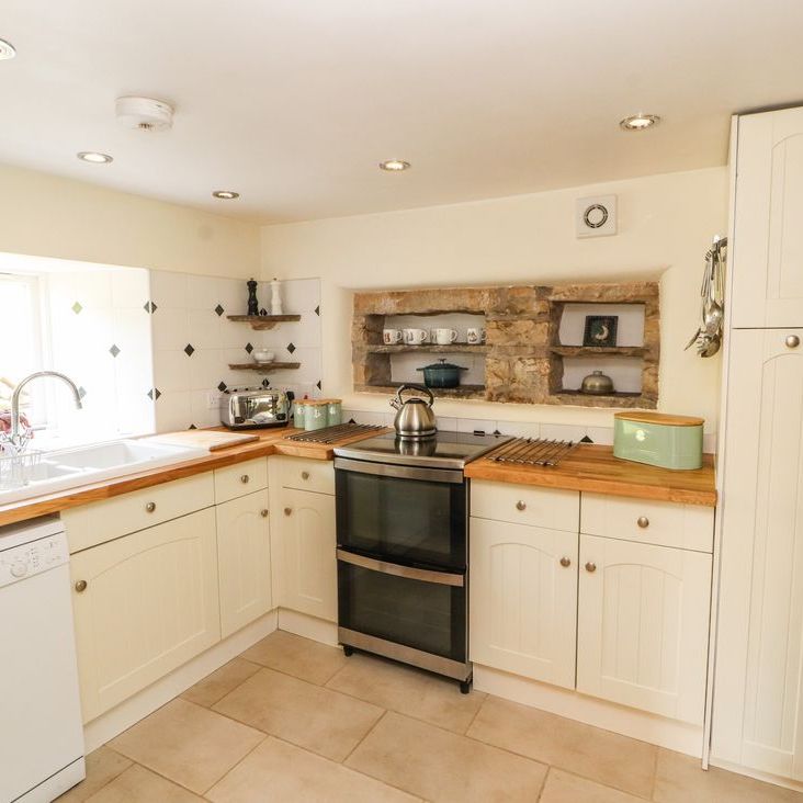 The kitchen at Roger Pot with cream cabinets, wooden worktops, a double oven and a stone shelving alcove