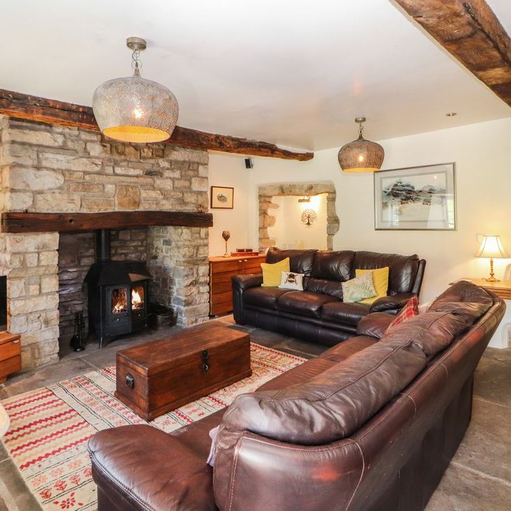 The Roger Pot living room with two leather sofas, a lit wood-burning stove and a flagstone floor