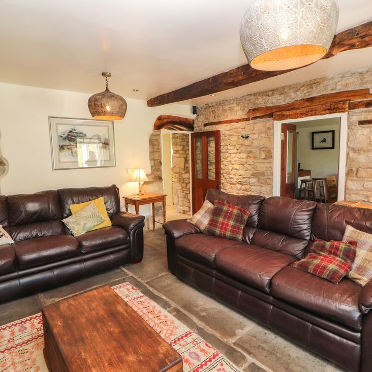 Two brown leather sofas around a wooden coffee table in the stone-walled living room at Roger Pot