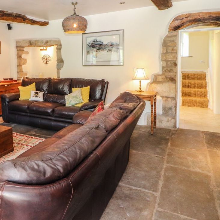 The Roger Pot living room with two leather sofas, exposed stone walls and an arched doorway to the staircase