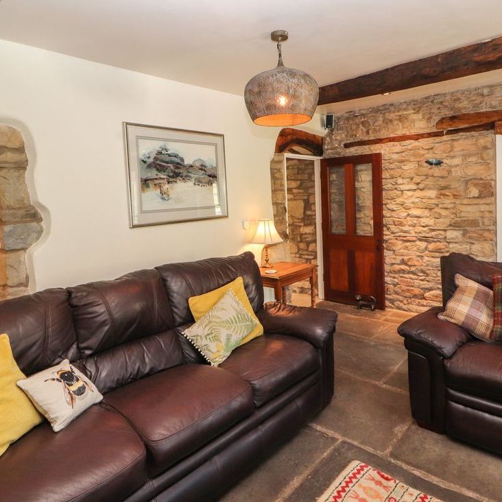 Two leather sofas with bright cushions in the beamed, stone-walled living room at Roger Pot