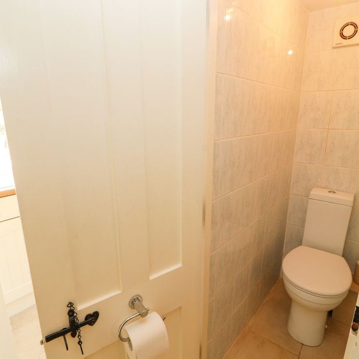 A compact tiled WC at Roger Pot with a white toilet and a toilet-roll holder on the door