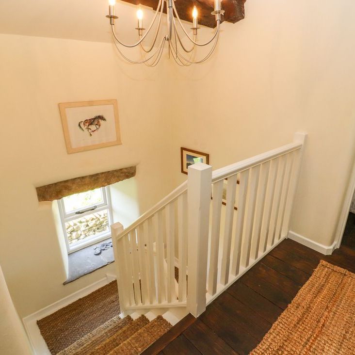 The staircase landing at Roger Pot with a white banister, woven runner, framed horse print and chandelier