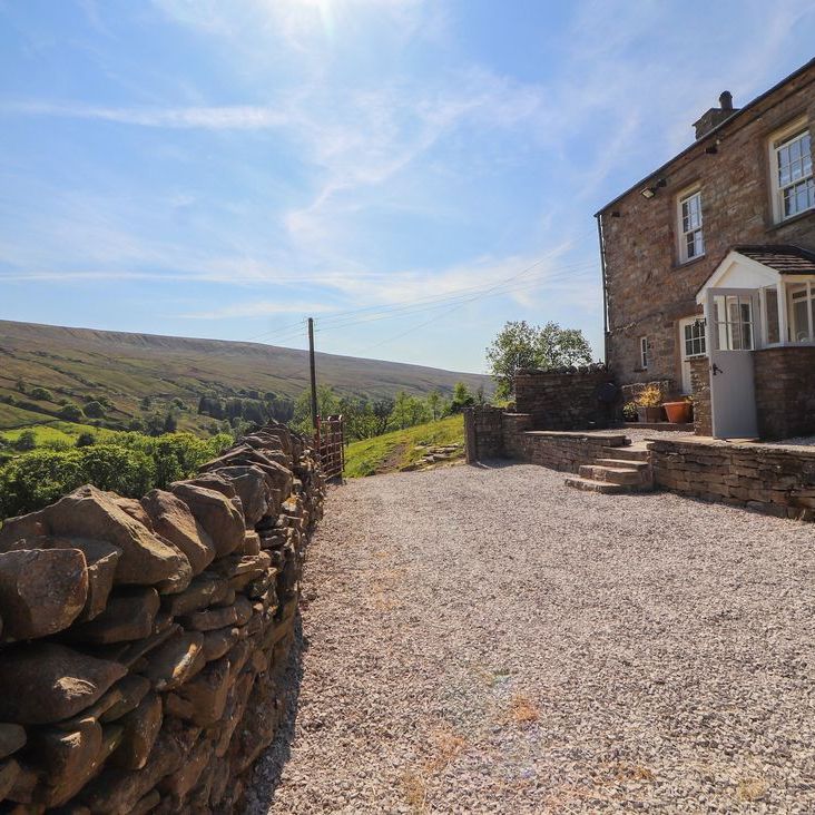Roger Pot stone cottage beside a gravel driveway and dry-stone wall, overlooking a green valley