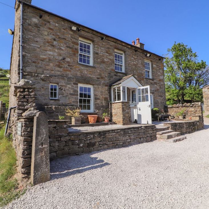 The stone front of Roger Pot with its white porch, potted plants and gravel driveway in sunshine