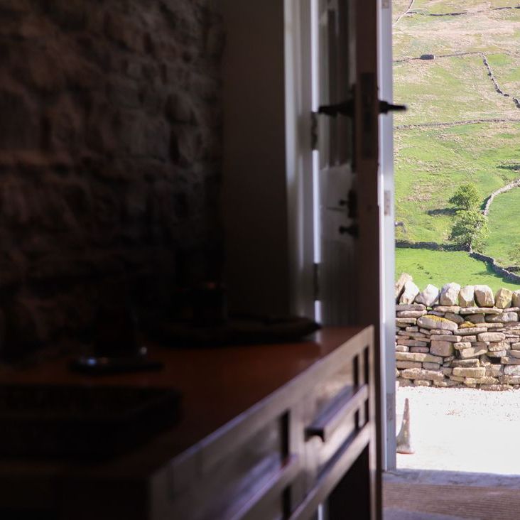 Looking out from a stone-walled room at Roger Pot through an open door to green hillside fields