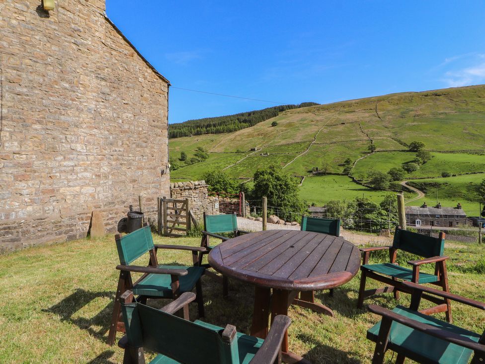 An outdoor seating area with a wooden round table and six chairs on grass near a stone building at Roger Pot in Garsdale near Sedbergh
