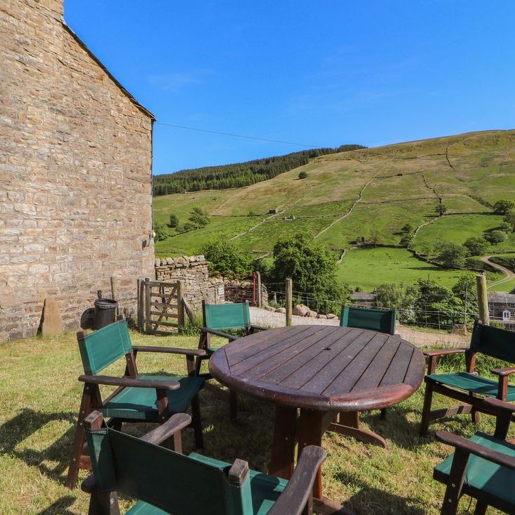 A round wooden table and six chairs on the grass beside Roger Pot, with valley views beyond