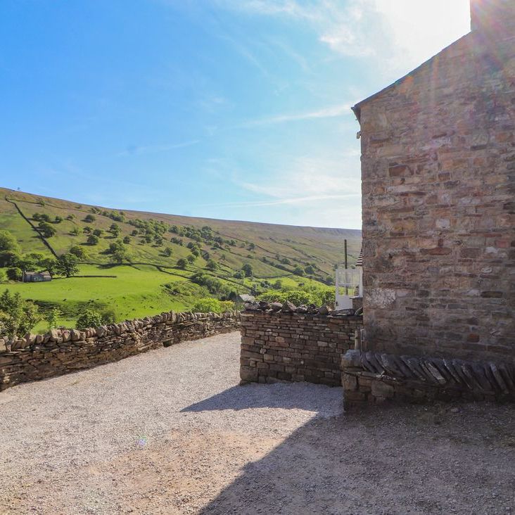 A gravel yard and dry-stone walls beside the stone building at Roger Pot, looking out to green hills