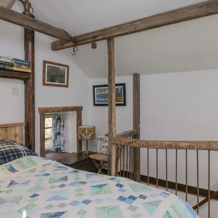A rustic loft bedroom at The Old Cart House with a patchwork quilt, a book shelf, beams and a stag picture