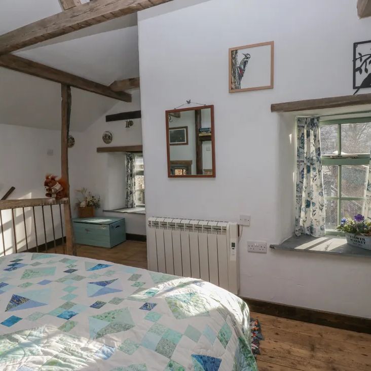 A bright beamed bedroom at The Old Cart House with a patchwork quilt, floral curtains and a toy squirrel on the rail