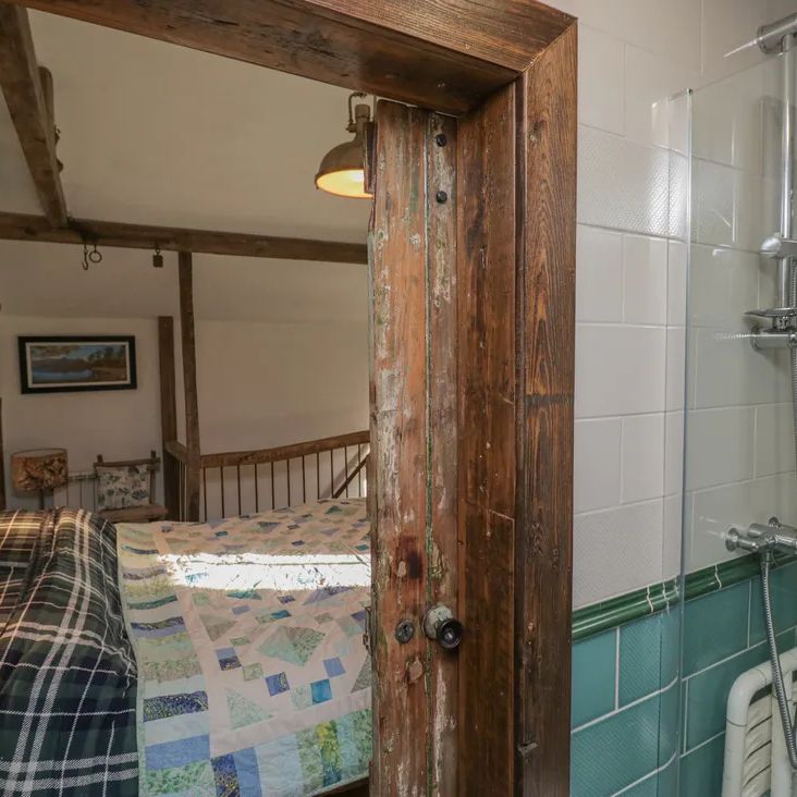 Looking through a rustic wooden door at The Old Cart House into a beamed bedroom with a blue patchwork quilt