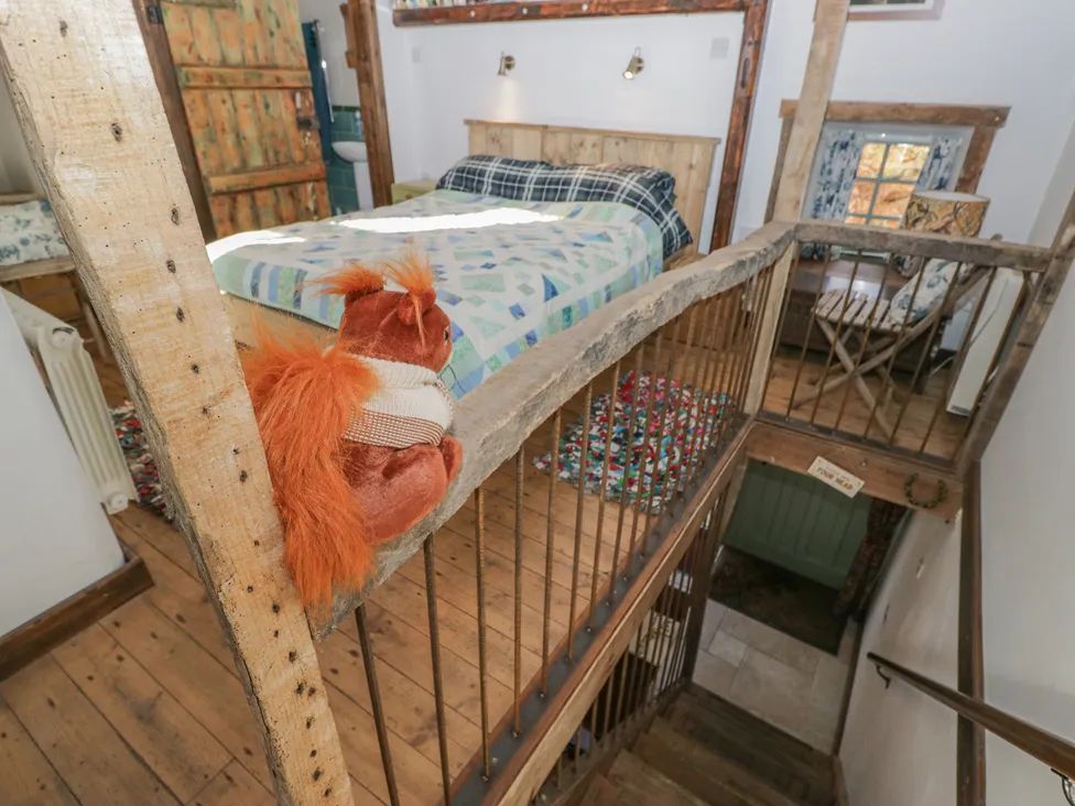 A bedroom with a bed covered in a patterned quilt a toy squirrel on the wooden railing and stairs leading down at The Old Cart House in Garsdale near Sedbergh