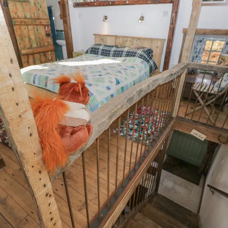 A mezzanine bedroom at The Old Cart House with a patchwork quilt, a toy squirrel on the rail and stairs descending below