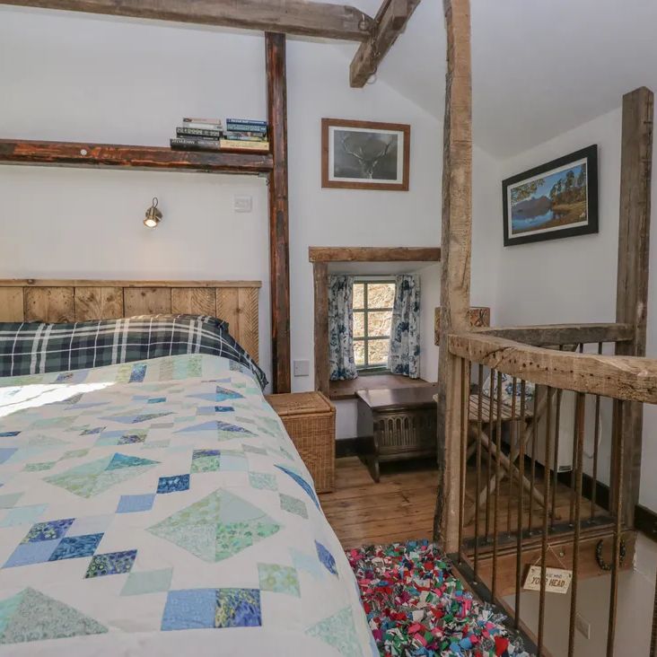 A rustic loft bedroom at The Old Cart House with a wooden bed, patchwork quilt, book shelf and stag picture