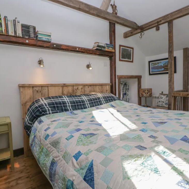 A sunny bedroom at The Old Cart House with a plank-headboard bed, patchwork quilt and book shelf above