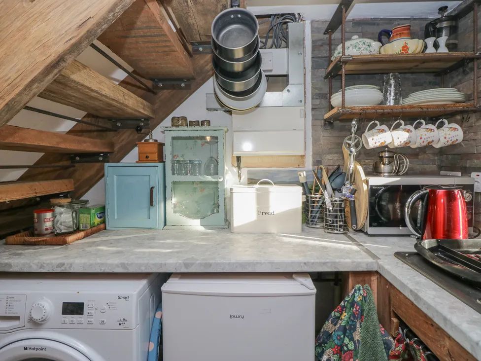 A kitchen corner with a countertop holding a small blue cabinet glassware bread box microwave red kettle and hanging pans and cups at The Old Cart House in Garsdale near Sedbergh