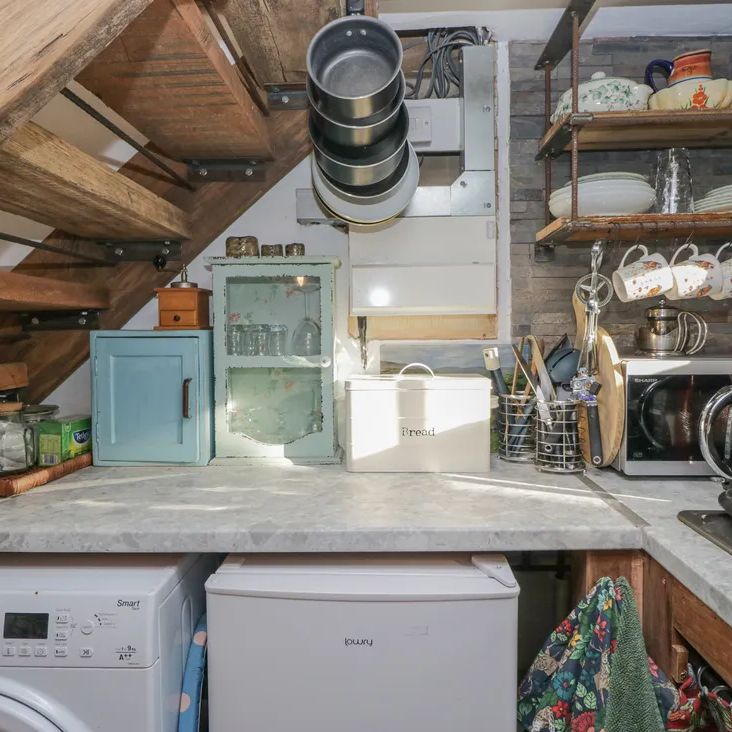 A rustic kitchen corner at The Old Cart House with vintage cabinets, open shelves of crockery and a red kettle