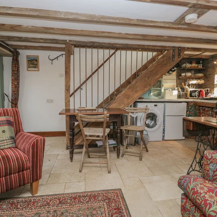 The open-plan living and dining area at The Old Cart House with striped and floral sofas, a dining table and staircase