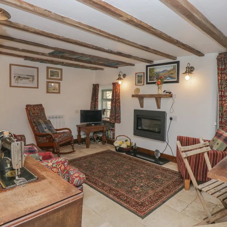 A cosy beamed living room at The Old Cart House with floral and striped seating, a wood-burning stove and Singer sewing machine