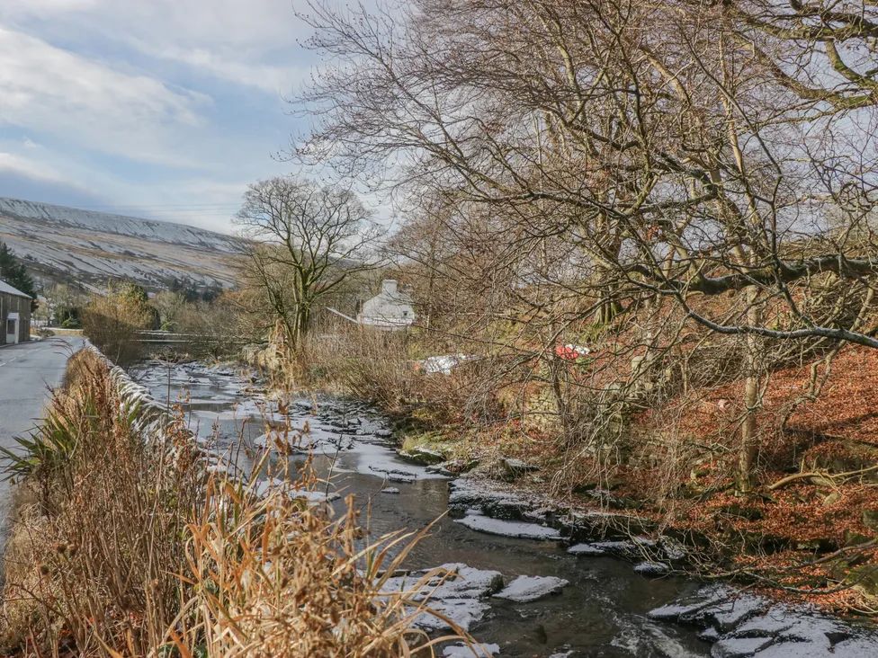 A river flowing alongside a road with leafless trees and a house in the background at The Old Cart House in Garsdale near Sedbergh