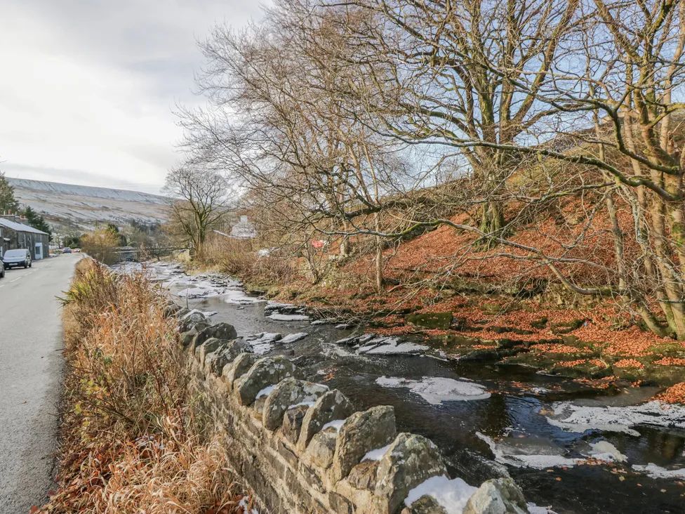 A road running alongside a stone wall and a partially frozen stream with leafless trees at The Old Cart House in Garsdale near Sedbergh