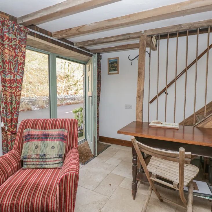 A room at The Old Cart House with a red striped armchair by an open garden door and a wooden staircase