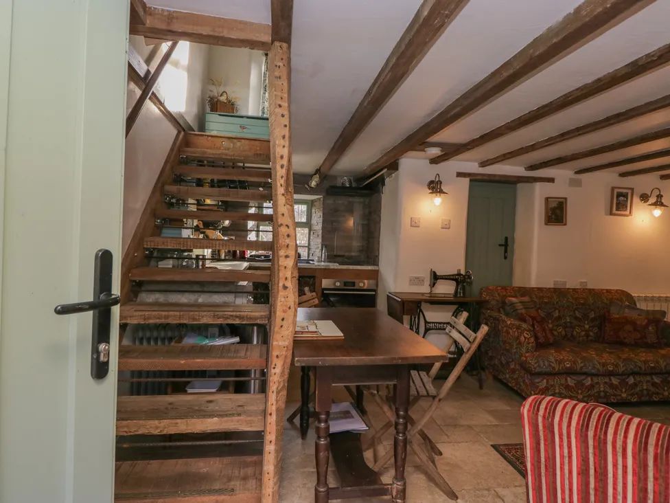 A rustic living area with wooden staircase, dining table with chairs, floral sofa, and vintage sewing machine at The Old Cart House in Garsdale near Sedbergh